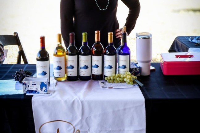 Smiling woman at a table with Bluegrass Vineyard wines displayed outdoors.