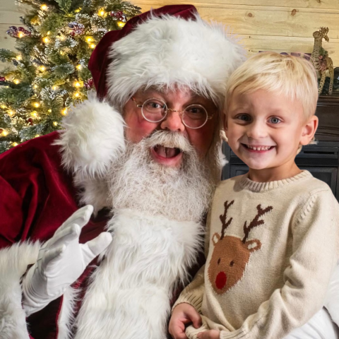 Child with Santa Claus in front of a decorated Christmas tree.